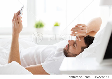 young man with smartphone in bed in morning young man with smartphone in bed in morning 35228544