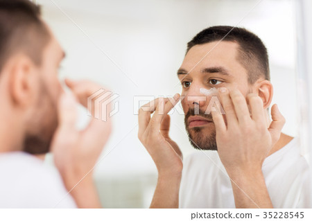 young man applying cream to face at bathroom young man applying cream to face at bathroom 35228545