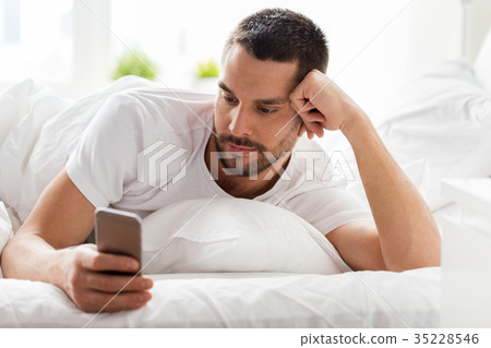 young man with smartphone in bed in morning 35228546