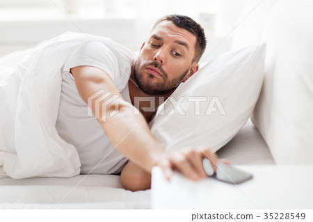 young man reaching for smartphone in bed 35228549