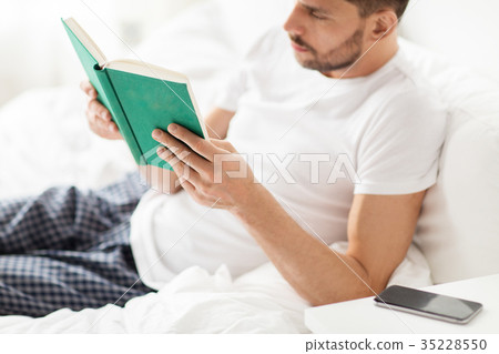 man reading book in bed at home man reading book in bed at home 35228550