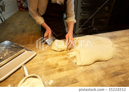 baker portioning dough with bench cutter at bakery 35228552