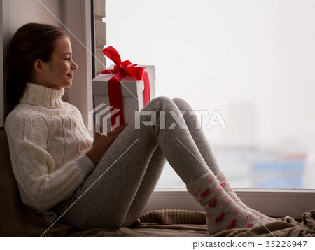 girl with gift sitting on sill at home window 35228947