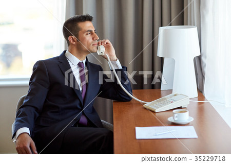 businessman calling on desk phone at hotel room businessman calling on desk phone at hotel room 35229718
