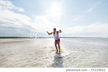 young man riding on skimboard on summer beach young man riding on skimboard on summer beach 35229832