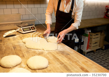 baker portioning dough with bench cutter at bakery baker portioning dough with bench cutter at bakery 35230700