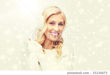 smiling young woman in winter earmuffs and sweater 35230873