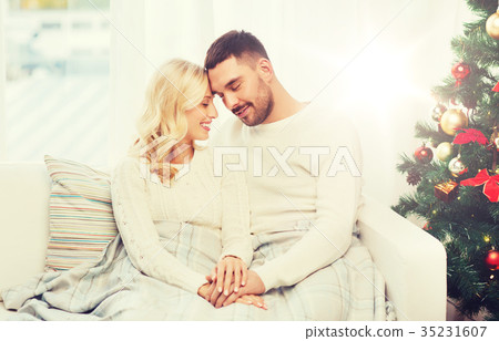 happy couple covered with plaid on sofa at home 35231607