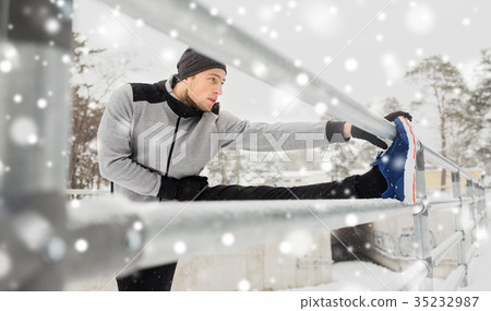 sports man stretching leg at fence in winter 35232987
