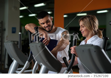 Middle aged woman working out in gym with coach 35267100