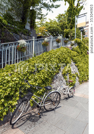 Two bicycles on footpath beside stone wall of ivy 35304903