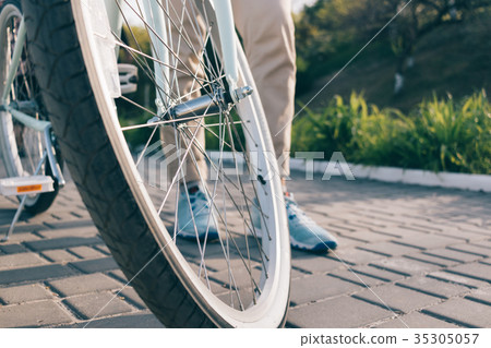 Wheel of a bicycle and female feet in sneakers Wheel of a bicycle and female feet in sneakers 35305057