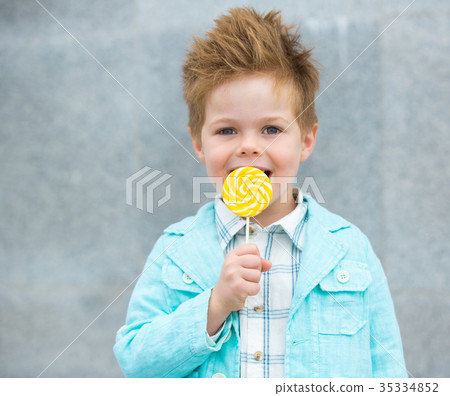 Fashion kid with lollipop near gray wall Fashion kid with lollipop near gray wall 35334852