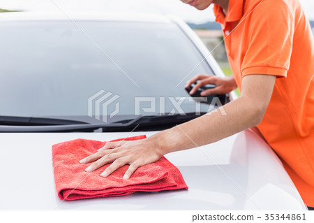 Young man using red microfiber cloth cleaning body of new silver car. For car maintenance concept.. Young man using red microfiber cloth cleaning body of new silver car. For car maintenance concept.. 35344861