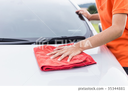 Young man using red microfiber cloth cleaning body of new silver car. For car maintenance concept.. 35344881