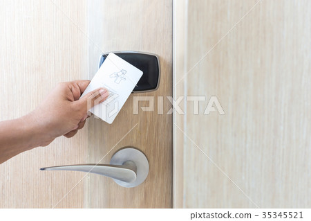 Hand holding white hotel key card in front of electric door Hand holding white hotel key card in front of electric door 35345521
