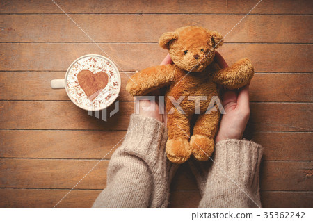 Woman holding teddy bear toy near cup of coffee 35362242