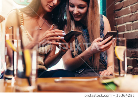 Two cheerful girlfriends using phone looking at 35364285