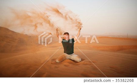 The guy throws sand over himself in the desert The guy throws sand over himself in the desert 35382208