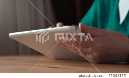 Close up of a white tablet PC in aged woman hands Close up of a white tablet PC in aged woman hands 35398155