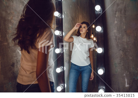 Sexy woman in a white t-shirt looks in the mirror 35413815