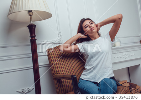 Attractive girl in a white t-shirt sits on a chair Attractive girl in a white t-shirt sits on a chair 35413876