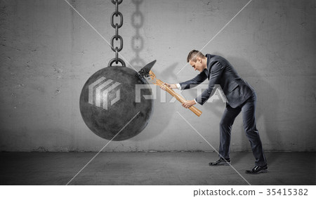 A small businessman hits a large solid iron ball 35415382