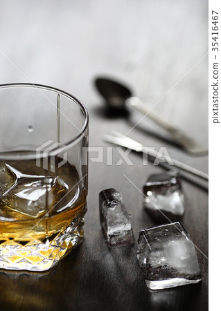 Whiskey in a glass and pieces of ice on a wood Whiskey in a glass and pieces of ice on a wood 35416467