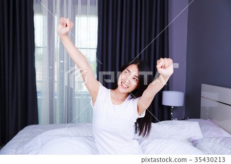 Woman waking up and hand raised on bed in bedroom 35430213