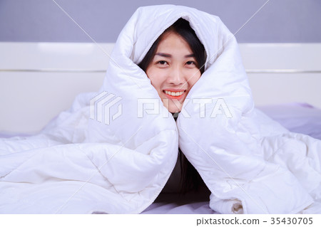 happy woman hiding under blanket on bed in bedroom 35430705