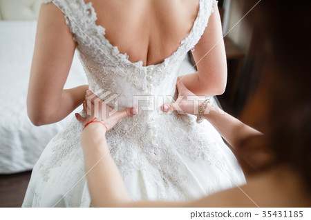 Bridesmaid is helping the bride to dress 35431185