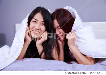 two woman hiding under blanket on bed in bedroom two woman hiding under blanket on bed in bedroom 35433233