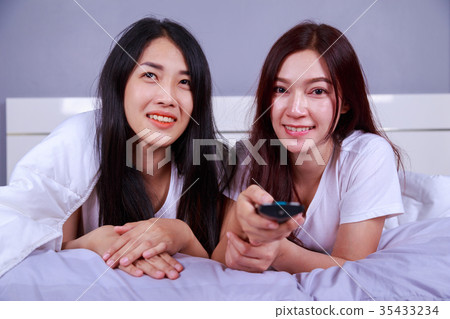 two best friends watching tv with remote on bed in bedroom two best friends watching tv with remote on bed in bedroom 35433234