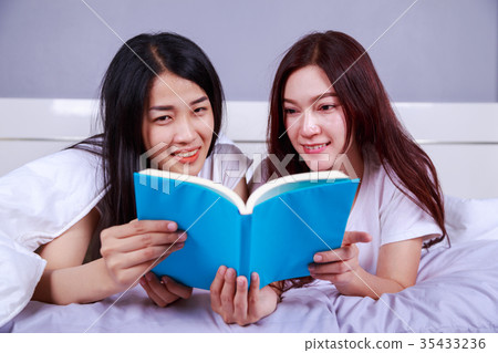 two woman reading a book on bed in bedroom two woman reading a book on bed in bedroom 35433236