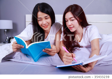 two woman writing and reading a book on bed in bedroom two woman writing and reading a book on bed in bedroom 35433239