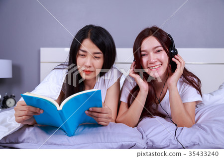 two woman reading a book and using smart phone on bed in bedroom two woman reading a book and using smart phone on bed in bedroom 35433240