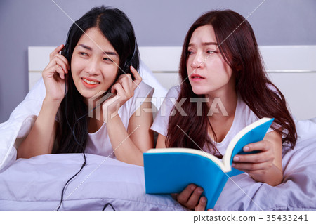 two woman reading a book and using smart phone on bed in bedroom 35433241