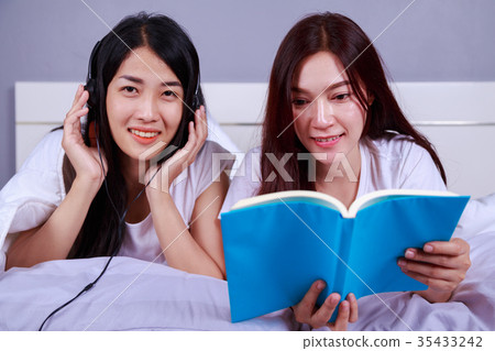 two woman reading a book and using smart phone on bed in bedroom two woman reading a book and using smart phone on bed in bedroom 35433242