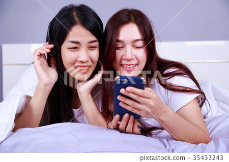 two woman using a phone in her hand on bed in bedroom two woman using a phone in her hand on bed in bedroom 35433243