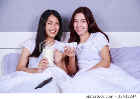 two best friends watching tv with remote and drinking a cup of c 35433244
