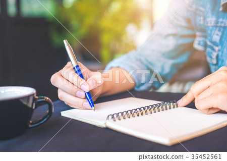 Woman hand is writing on a note pad with a pen Woman hand is writing on a note pad with a pen 35452561