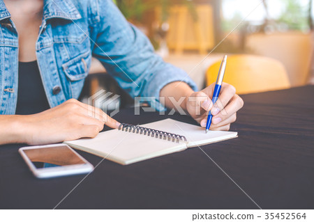 Woman hand is writing on a note pad with a pen. 35452564