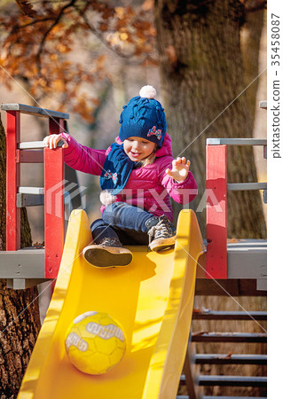 Happy three-year baby girl in jacket on slide Happy three-year baby girl in jacket on slide 35458087