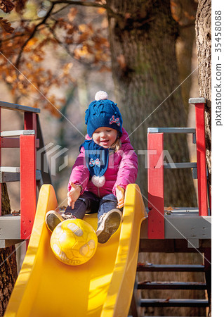 Happy three-year baby girl in jacket on slide Happy three-year baby girl in jacket on slide 35458088