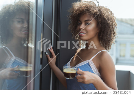 Cheerful african woman tasting mug of beverage Cheerful african woman tasting mug of beverage 35481004