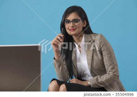 Businesswoman holding pen by laptop at desk  35504996