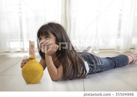 Little girl thinking lying on floor with piggy bank 35504998