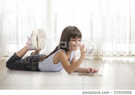 Little girl lying on floor looking in money box Little girl lying on floor looking in money box 35505008