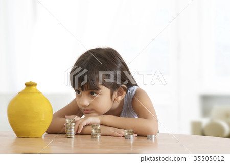 Girl leaning on table looking at piggy bank and stack of coins 35505012