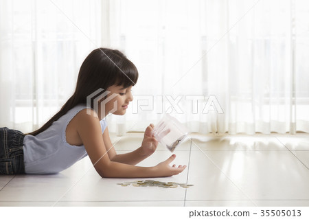 Little girl lying on floor looking in money box 35505013